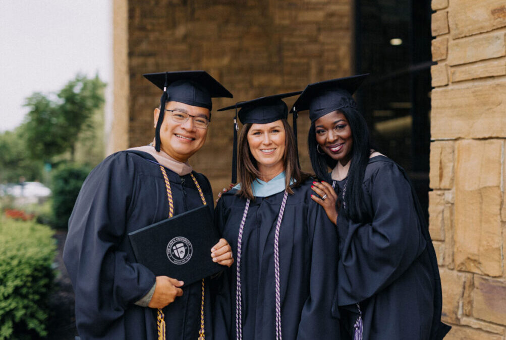 Three seminary students at graduation pose for a photo in their caps and gowns.